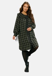 Schwarz-grünes kariertes Kleid mit Kragen, durchgehender Knopfleiste und elastischen Bündchen. Es hat seitliche Bindeüsen und eine lockere, knielange Passform.