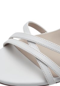 Bílé sandály s kříženými pásky vyrobené z hladké kůže, s neutrální vnitřní stélkou a minimalistickými designovými prvky.