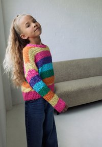 Multicolored sweater with textured, fuzzy fabric featuring horizontal stripes in pink, orange, purple, blue, green, and yellow. Jeans visible.