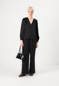 Blusa negra de manga larga con escote en V y detalle de botones, combinada con pantalones holgados negros. Los accesorios incluyen un pequeño bolso negro y zapatos de estampado animal.