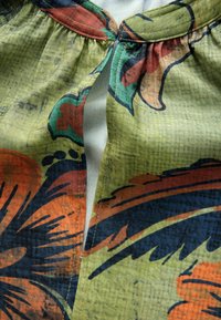 Stof met bloemenpatroon met grote oranje en blauwe bloemen op een groene achtergrond. Inclusief gerimpelde halslijn en centrale split.