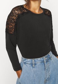 Top nero a maniche lunghe con spalle in pizzo, tessuto morbido, scollatura rotonda, abbinato a pantaloni shorts in denim a vita alta.