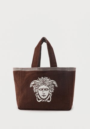 Bolso tote marrón con dos asas, con un diseño blanco de cabeza de Medusa centrado en el frente.