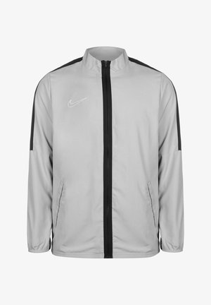 Giacca Nike grigia chiara con zip nera e pannelli laterali. Presenta un alto colletto e polsini elasticizzati; tessuto morbido e leggero.