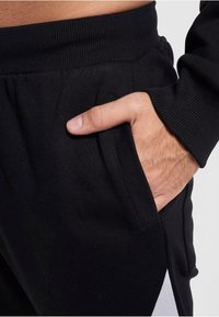 Schwarze sportliche Jogginghosen mit einem gerippten Bund und Seitentaschen, versehen mit einem kontrastierenden weißen Paneelakzent an der Seite.