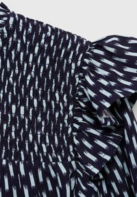 Mörkblått tyg med ljusblå penseldragmönster, med smock och en volangkant. Texturerat och något elastiskt.