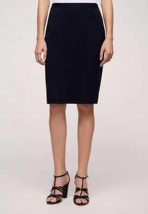 Jupe navy à mi-genou en tissu doux avec une silhouette ajustée. Associée à des sandales à talons hauts noires à lanières, rehaussant le look.