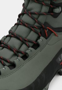 Roheline matkajalats, millel on tekstureeritud pind, mustad ja punased paelad, väljendunud tallad ning tugevdatud servad vastupidavuseks.