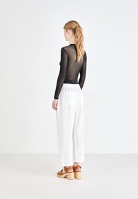Black sheer long-sleeve top paired with loose white pants. The model wears brown strappy heels, showcasing a minimalistic design.
