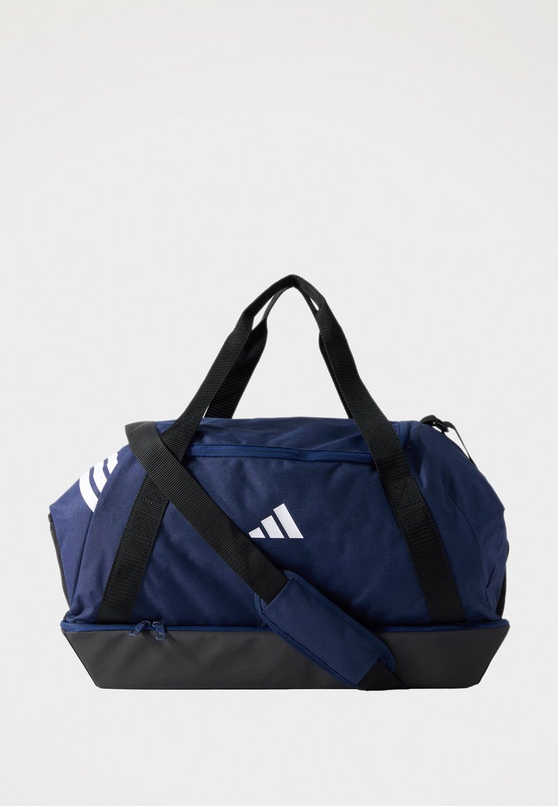 Τσάντα duffel σε ναυτικό μπλε και μαύρο με μαύρες λαβές και ριχτάρι ώμου, λευκό λογότυπο Adidas και φερμουάρ σε απλό φόντο.