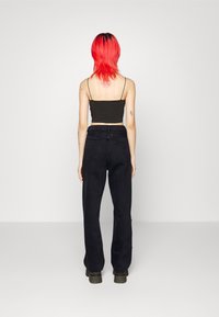 Svarta vida byxor med hög midja, tillsammans med en figurnära svart crop top. Modellen har röd hår och visar upp en minimalistisk stil.