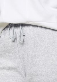 Calças de moletom cinzentas com uma textura suave, apresentando um fio de ajuste na cintura com borlas cinzentas claras, combinadas com um hoodie de fleece branco.