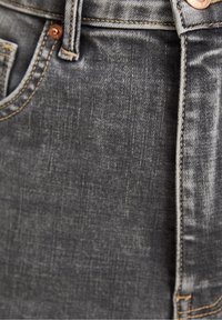 Šedé džíny z denimu s mírně vybledlým povrchem, viditelným šitím a měděným knoflíkem v oblasti přední kapsy.