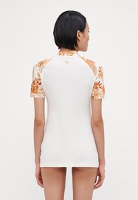 Short-sleeve rash guard in white with floral pattern accents in orange and yellow on shoulders. Smooth, stretch fabric for comfort.