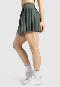 Falda plisada verde con cintura alta, hecha de tela suave. Combinada con zapatillas blancas y calcetines con letras en negro.