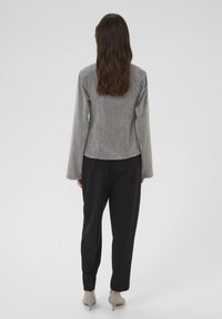 Grå kordfløjl langærmet top med en rund kant, parret med løse sorte bukser, båret med lysebeige hæle. Glat tekstur.