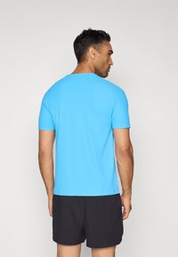Hellblaues T-Shirt mit kurzen Ärmeln und Rundhalsausschnitt, glatte Textur, taillierter Schnitt, getragen mit schwarzen Shorts, Rückansicht.