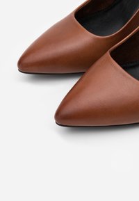 Ballerines en cuir marron à bout pointu avec une texture lisse et une découpe basse près de l'ouverture, dotées d'une doublure intérieure noire.