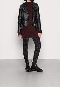 Chaqueta de motorista de cuero negro sobre un vestido suéter de punto burdeos, combinada con pantalones pitillo a cuadros negros y botines negros con paneles elásticos laterales.