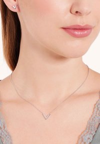 Zilveren sieraden bestaan uit een delicaate ketting met een V-vormige hanger en kleine accenten, gecombineerd met bijpassende V-vormige studoorbellen.