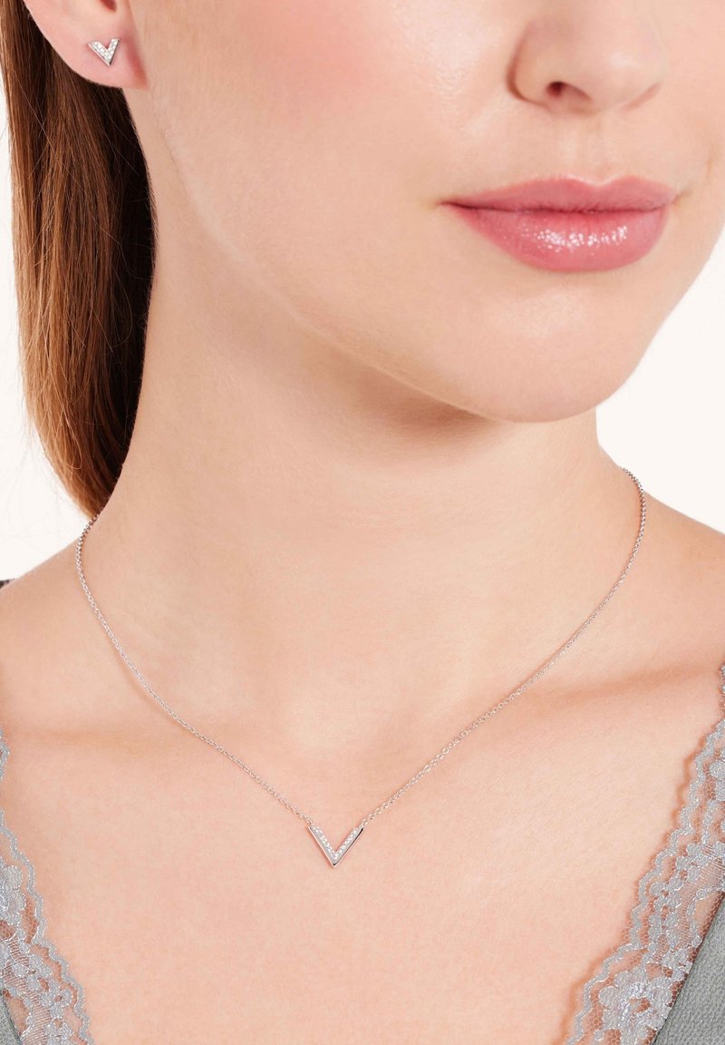 Zilveren sieraden bestaan uit een delicaate ketting met een V-vormige hanger en kleine accenten, gecombineerd met bijpassende V-vormige studoorbellen.