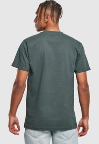 Mørkegrøn bomulds t-shirt med korte ærmer og rund halsudskæring. Har et enkelt design på bagsiden og en afslappet pasform, kombineret med lyse jeans.