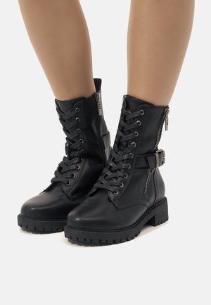 Botas de cuero negro hasta el tobillo con cordones en la parte delantera y cremallera lateral, que cuentan con un detalle de hebilla y suelas de goma texturizadas para mayor agarre.