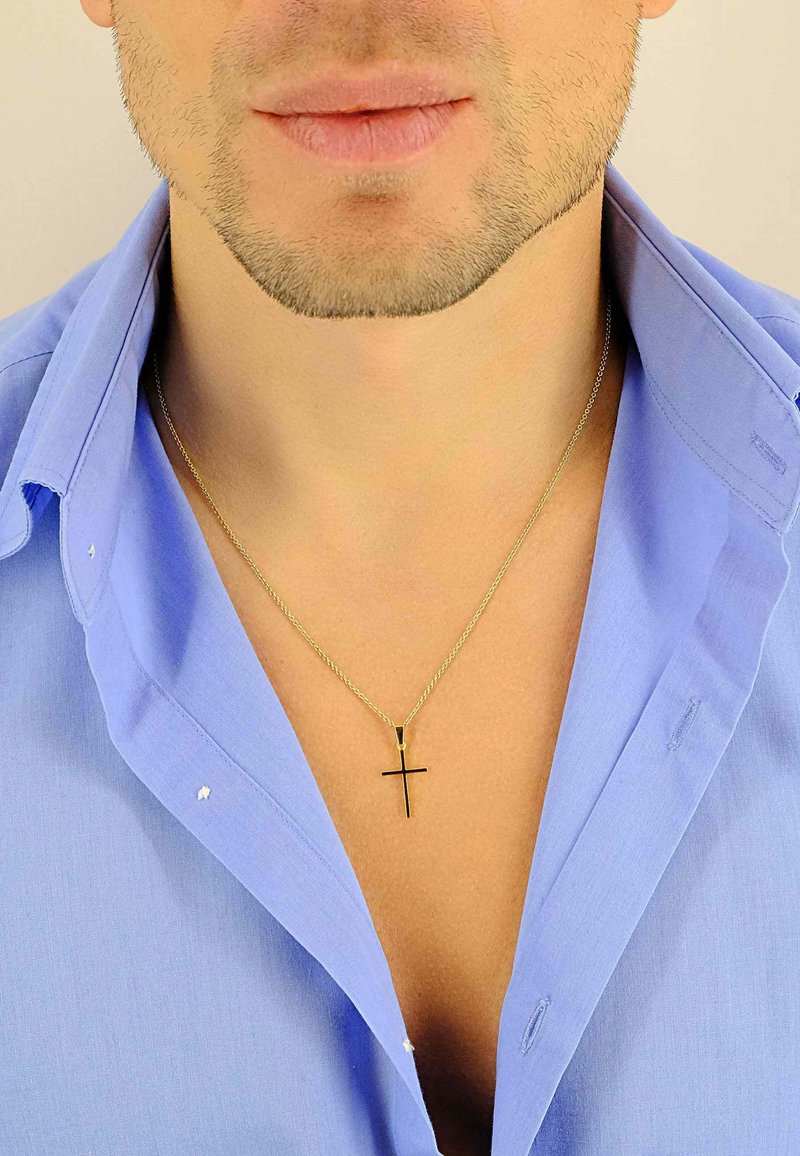 Collier chaîne en or avec un pendentif croix noire, porté sur une chemise bleu clair déboutonnée. Présente une texture métallique lisse et des maillons réguliers.