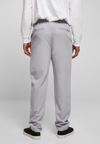 Helle graue Jogginghose mit einem elastischen Bund, Seitentaschen und einer glatten Textur, kombiniert mit schwarzen Slippers.