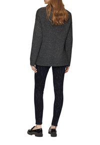 Szary sweter dzianinowy o luźnym kroju z prążkowanym dołem, zestawiony z ciemnoniebieskimi legginsami w wężowy wzór i czarnymi lakierowanymi mokasynami.