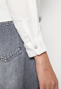 Witte blouse met lange mouwen en een gestructureerde afwerking, met een knoopsluiting bij de manchetten, gecombineerd met een grijze spijkerrok met een zak.