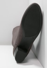 Botín de ante gris con una suela de goma negra texturizada y tacón bajo, que presenta una puntera redondeada y un diseño ajustado.