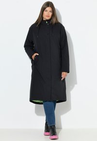 Dlouhý černý nepromokavý kabát s vysokým límcem, zapínáním na knoflíky a bočními kapsami. Má kontrastní zelený vnitřek a černé boty s růžovými podrážkami.