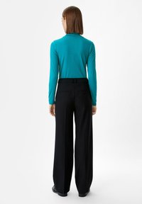 Szmaragdowa bluzka z długim rękawem i wysokim kołnierzem, w połączeniu z czarnymi spodniami o szerokich nogawkach w wysokim stanie. Gładki materiał i minimalistyczny design.