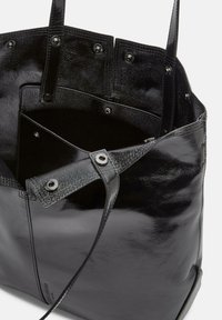 Czarna skórzana torba na ramię o błyszczącej powierzchni, z wieloma wewnętrznymi kieszeniami, zatrzaskami oraz płaskimi uchwytami.