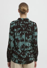 Långärmad skjorta i en teal och svart abstrakt mönster, med standardkrage, knappade manschetter och en avslappnad passform. Mjuk tygtextur.