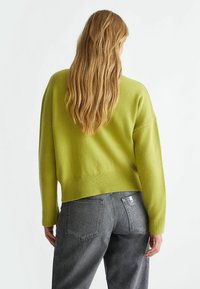 Maglione verde lavorato a maglia con un design cropped, orlo a costine e maniche lunghe, abbinato a jeans in denim grigi con una leggero lucido.