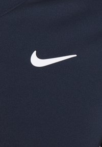 Camiseta deportiva Nike azul marino con un destacado logotipo de swoosh blanco en el frente, hecha de tela suave y elástica con una textura lisa.