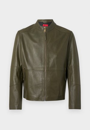 Kurtka skórzana w kolorze oliwkowej zieleni z wysokim kołnierzem, zamkiem błyskawicznym z przodu i dwoma zamykanymi kieszeniami bocznymi. Gładka faktura z przeszyciami jako detal.