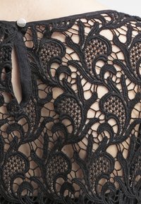 Tessuto di pizzo ricamato nero con motivi floreali, dotato di un'apertura a chiave e chiusura con bottone sul retro per un tocco di dettaglio.