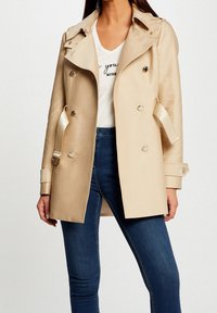 Beiger doppelseitiger Trenchcoat mit tailliertem Gürtel, silberner Beschläge und Schulterklappen; aus glattem, leichtem Stoff gefertigt.