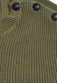 Maglione lavorato a maglia verde oliva con texture a coste, scollo rotondo e tre bottoni neri lungo la spalla.