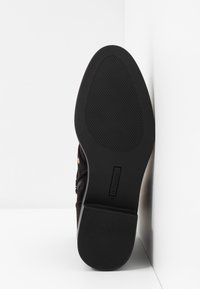 Zapato de ante negro con suela de goma texturizada, que presenta un detalle de cremallera y un pequeño acento metálico. La suela es lisa con patrones acanalados.