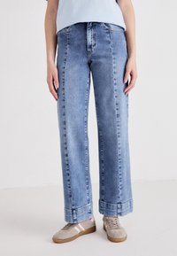 Jeans in denim azzurro chiaro a gamba larga con vita alta, caratterizzati da un davanti pulito, taglio dritto e orli ripiegati. Abbinati a sneaker beige.