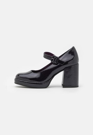 Zwarte lakleren Mary Jane schoen met een ronde neus, verstelbare band en een stevige hoge hak voor stabiliteit. Overal een gladde textuur.