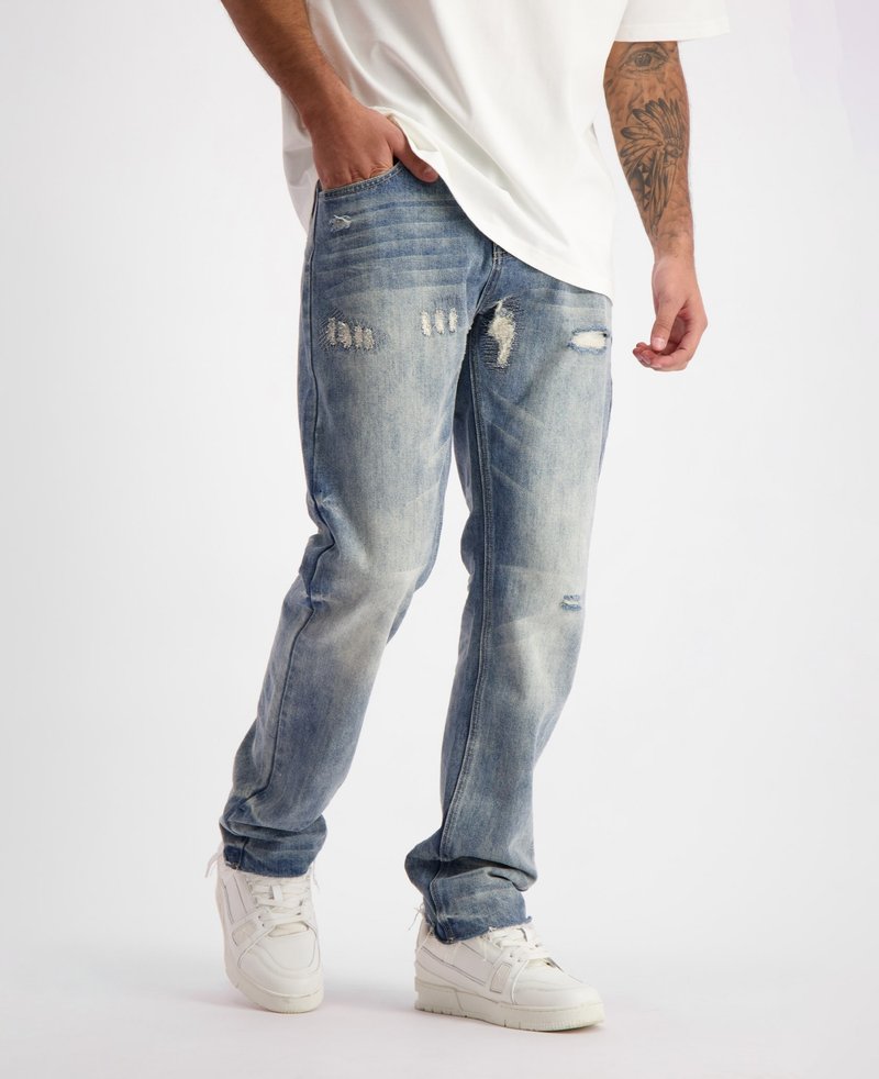 Lichtblauwe versleten denim jeans met zichtbare scheuren en vervaging, met een relaxed fit en vijf-pocket ontwerp, gecombineerd met witte sneakers.