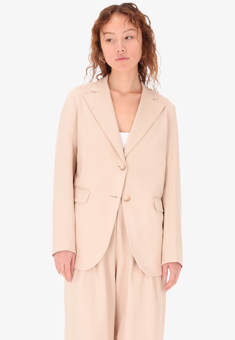 Blazer beige con rever a scialle, due bottoni e tasche laterali. Tessuto liscio con una vestibilità su misura e spacco singolo sul retro.
