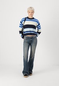 Knit sweater with blue and white stripes, round neckline, and cropped design, paired with flared dark jeans and black footwear.