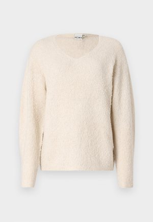 Ljusbeige tröja i mjukt, texturerat tyg. Har en V-ringning, långa ärmar och sidsprund för ökad rörelsefrihet. Enkel, minimalistisk design.