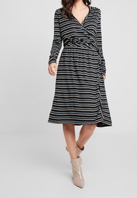 Zwarte, lange mouw wikkeljurk met horizontale strepen in lichtblauw en beige, cinched taille en een middelhoge rok. Heeft een zijsplit.